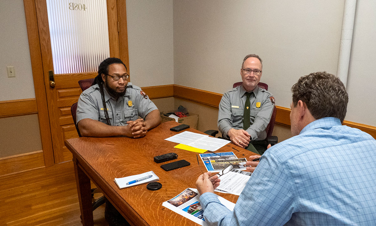 This is a photo of two Kansas park rangeres speaking with someone at table.